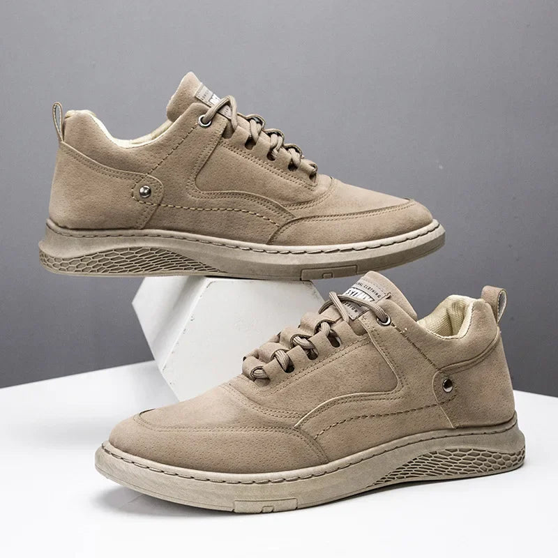 A pair of low-top casual sneakers in a light taupe suede-like material, displayed on a white geometric block against a gray background.