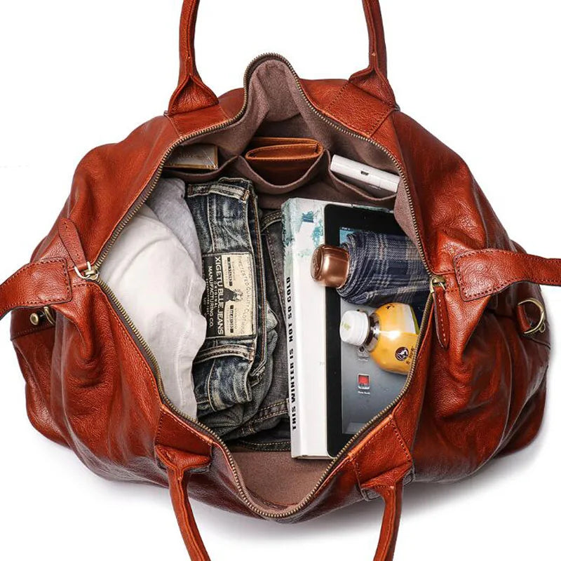 Brown leather bag with items like jeans, books, and a bottle inside on a white background