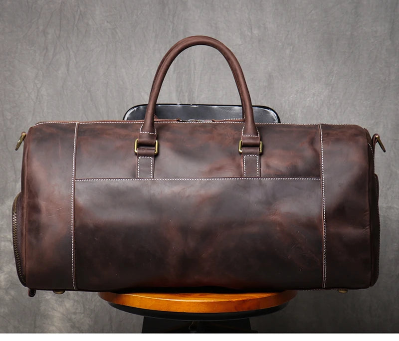 Brown leather duffel bag on a wooden stand with a gray background