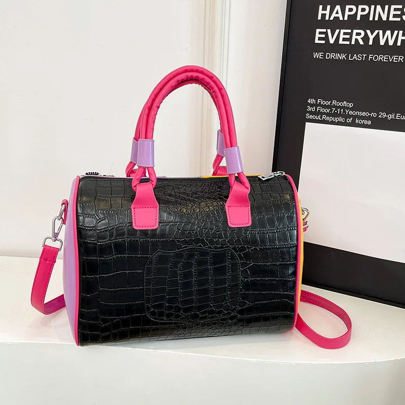 Black crocodile-patterned handbag with pink handles and strap on a white surface.