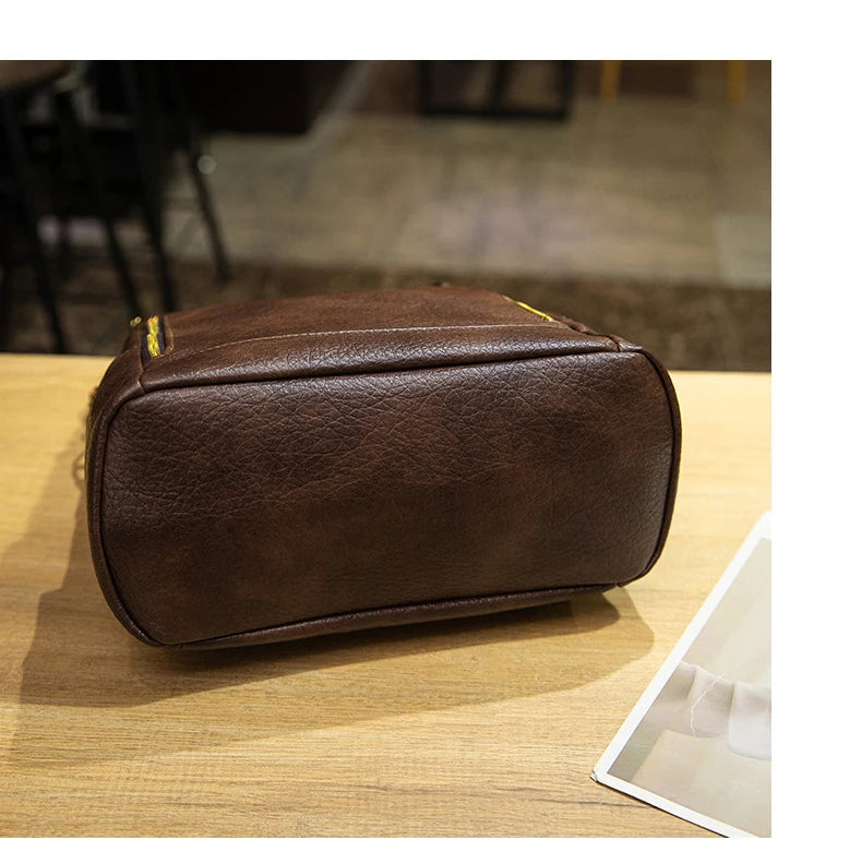 A dark brown textured faux-leather or leather cosmetic pouch with a yellow zipper pull, resting on a light wood tabletop.