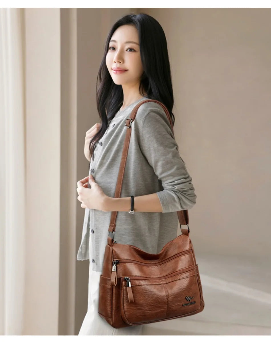Woman holding a brown leather shoulder bag against a neutral background