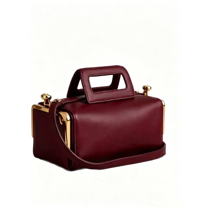 A burgundy leather cosmetic bag with a top handle, gold-tone hardware, and a detachable shoulder strap, shown on a plain white background.
