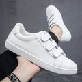 White sneakers with velcro straps worn by a person on a dark background