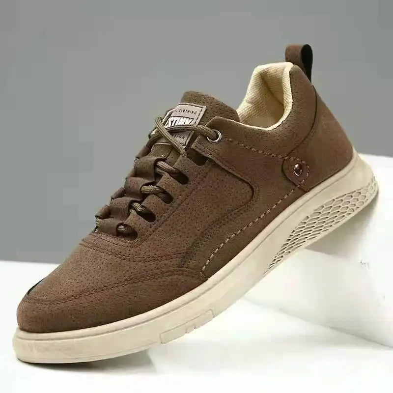 A brown low-top casual sneaker with a textured suede-like upper, matching brown laces, a beige interior lining, and a thick beige sole, shown resting on a white display block against a gray background.