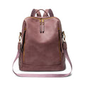 A dusty rose faux-leather backpack with gold-tone hardware, featuring a front zippered pocket, top zipper, dual top handles, and a detachable shoulder strap, shown against a plain white background.