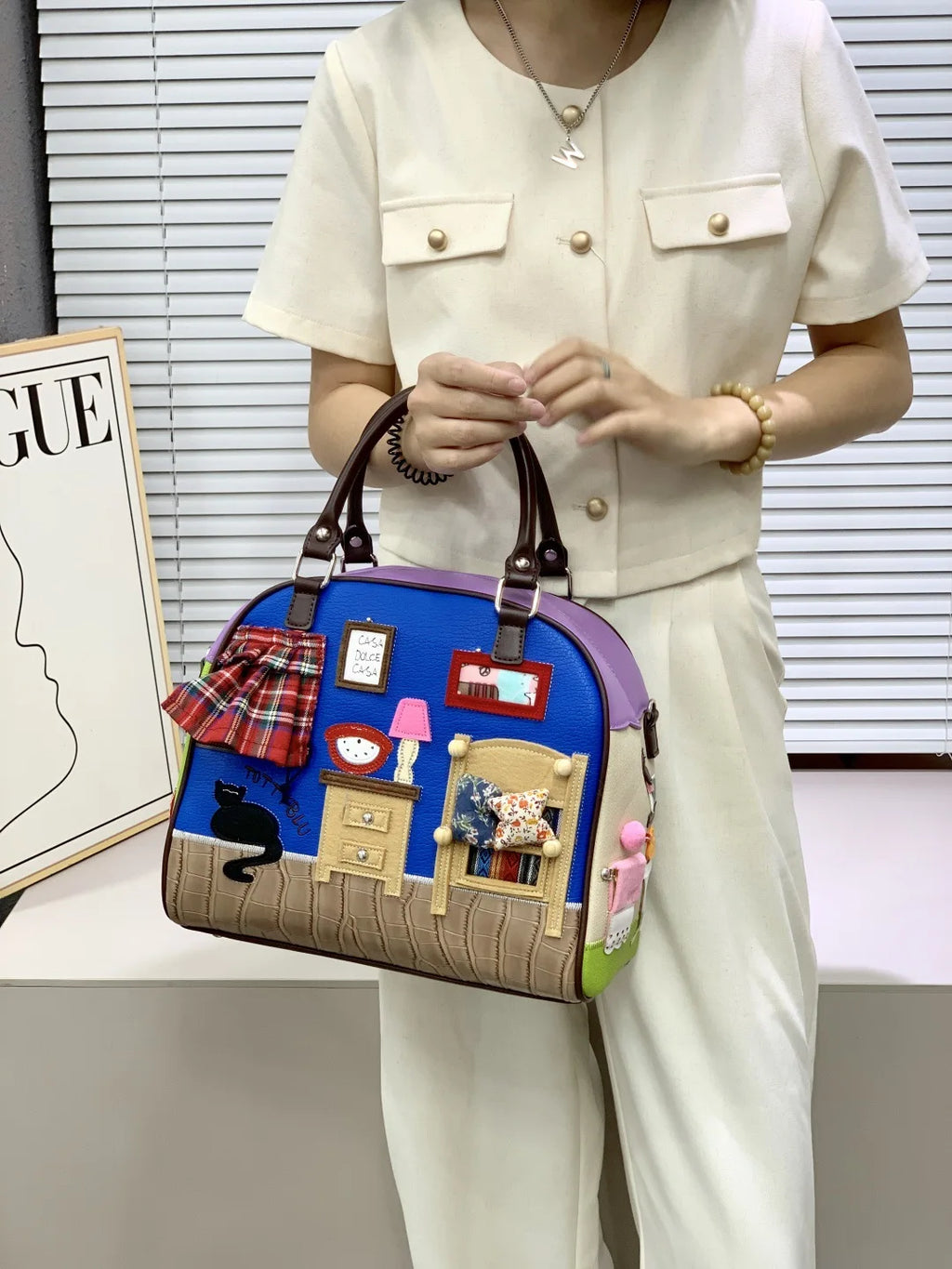 Person holding a colorful handbag with house design in an indoor setting