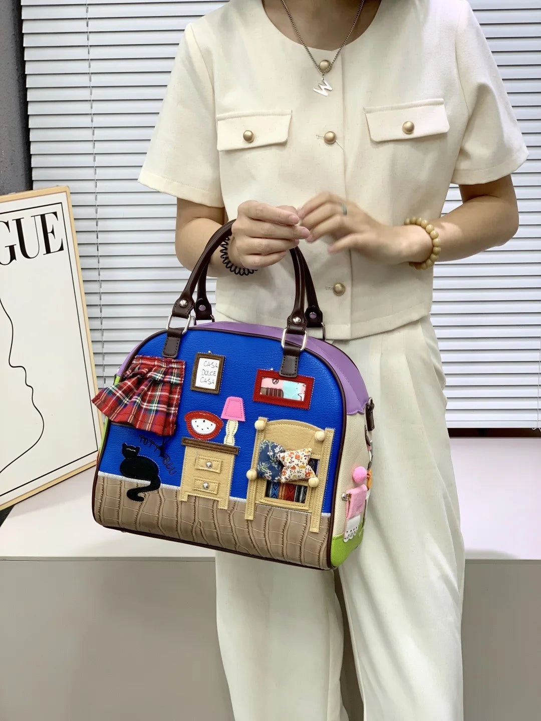 Person holding a colorful handbag with house design in an indoor setting