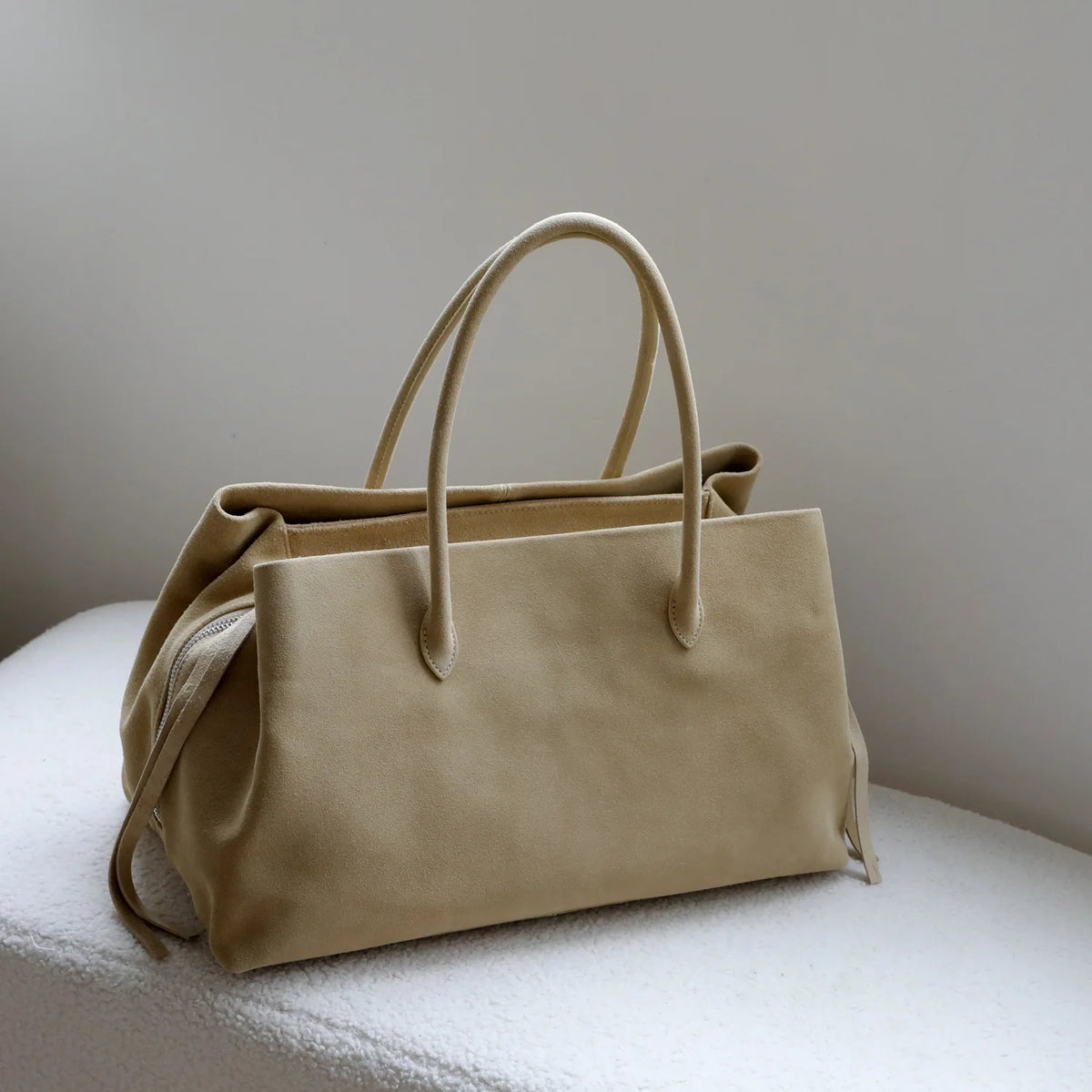 Beige handbag on a white surface with a neutral background