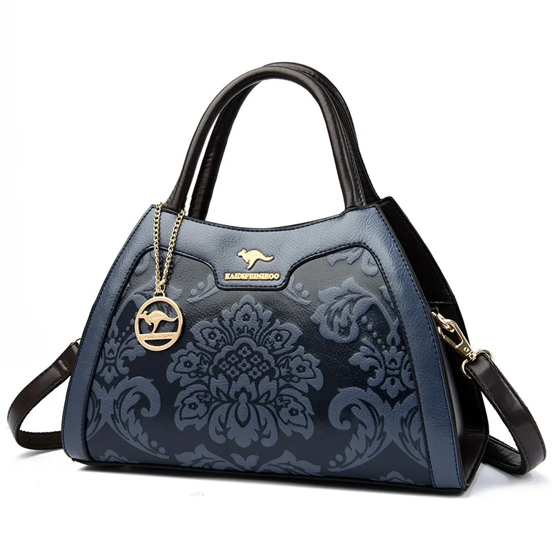 Blue patterned handbag with black handles and strap on a white background
