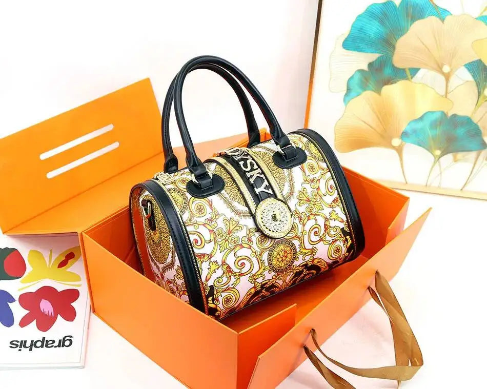 Decorative handbag with gold patterns in an orange box, with a floral card in the background.