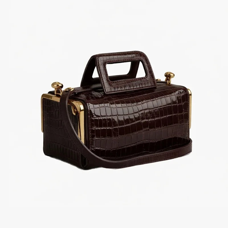 Brown crocodile-patterned handbag with gold accents on a white background