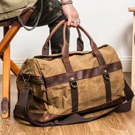 Waxed canvas duffel bag with leather straps held by a person sitting on a wooden stool.