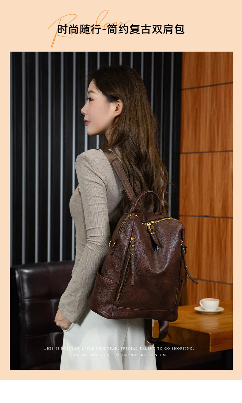 A woman wearing a brown pebbled leather backpack with gold-tone hardware, standing in a modern interior setting with wood paneling and a dark leather chair.
