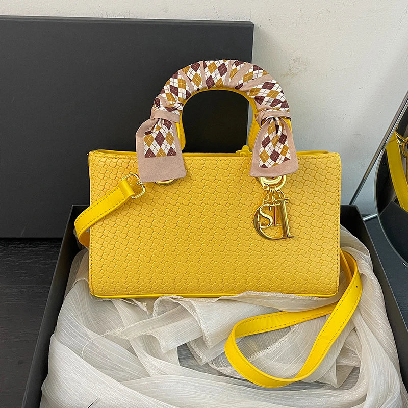 Yellow handbag with patterned handle and visible brand logo on a white fabric background