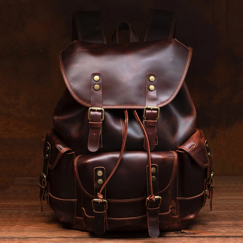 A dark brown leather backpack with multiple front pockets, brass-tone hardware, and drawstring details, photographed against a dark brown textured background.