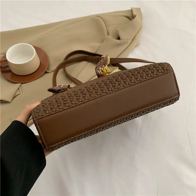 Brown woven handbag held by a person with a beige jacket and cup in the background