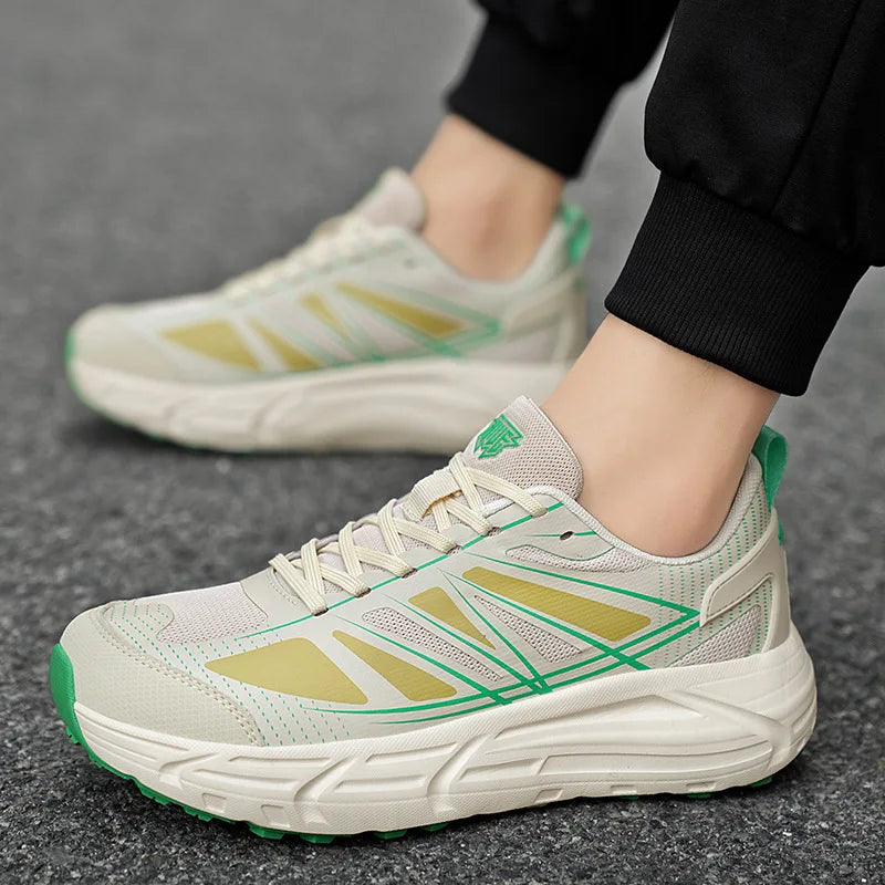 A close-up of a person wearing a pair of athletic sneakers on a gray pavement surface. The shoes are off-white with metallic gold geometric accents and bright green details, including the tongue logo and outsole edges.