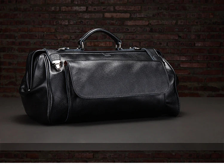 Black leather duffel bag on a dark surface with a brick wall background
