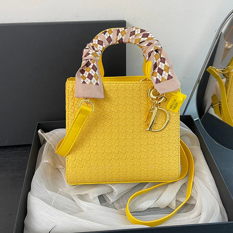 Yellow handbag with a decorative handle and visible brand logo, placed on a white surface.