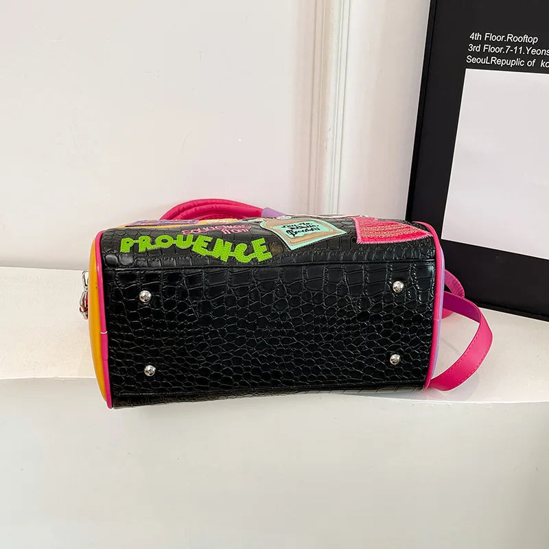 Black handbag with pink straps and green text on a white surface