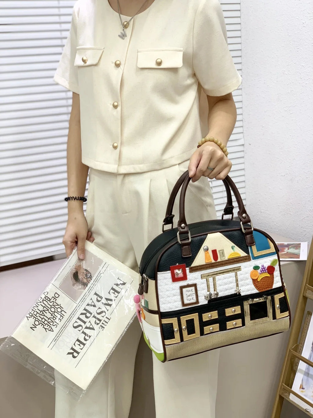 Person holding a decorative handbag with artistic design, wearing a beige outfit.
