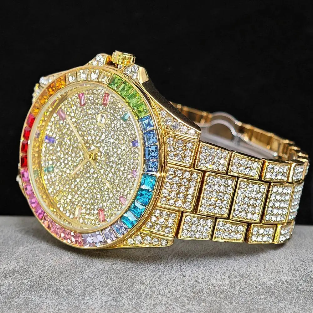 A gold-tone wristwatch with a diamond-encrusted face and a colorful rainbow bezel, resting on a gray textured surface against a black background.