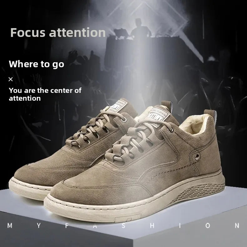 A pair of low-top casual sneakers in taupe suede with cream soles, displayed on a light gray platform against a dark stage-like background with spotlighting and promotional text.
