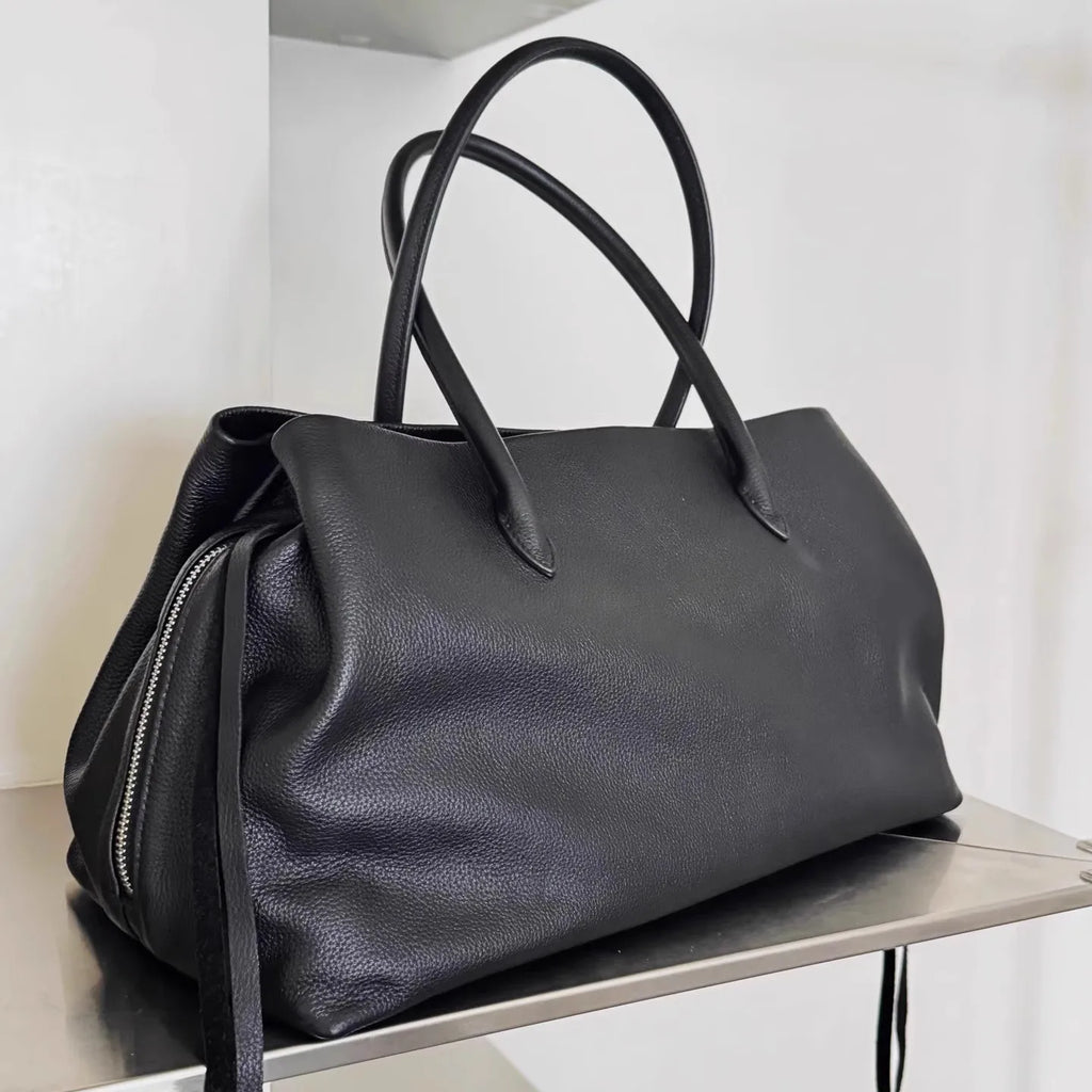 Black leather handbag on a metallic surface with a white background
