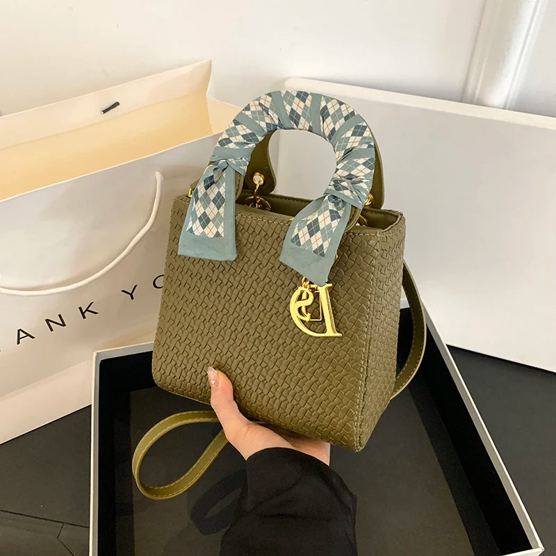 Green handbag with a decorative ribbon held by a hand, with a 'DKNY' branded box in the background.