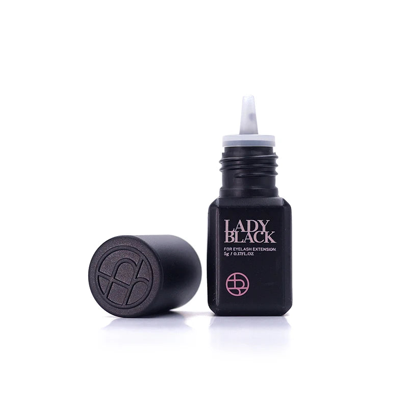 A bottle of Lady Black Fire Eyelash Enhancer with its cap off and standing beside it, on a clean white background.