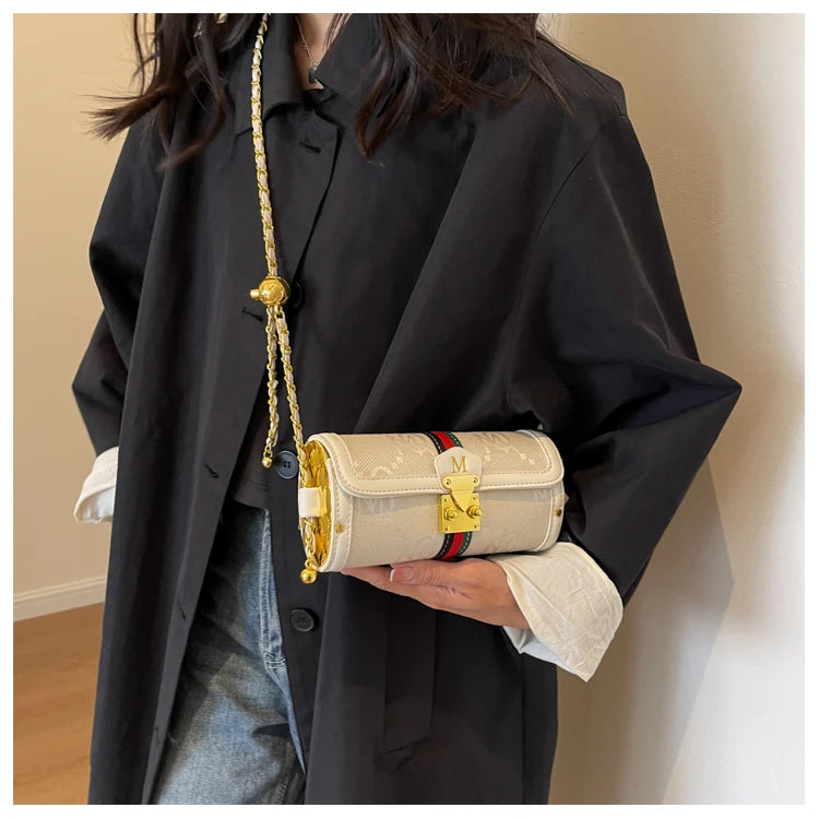 A person wearing an oversized black blazer and light blue jeans holds a cream-colored Gucci shoulder bag with gold hardware, a gold chain strap, and the signature red and green web stripe.
