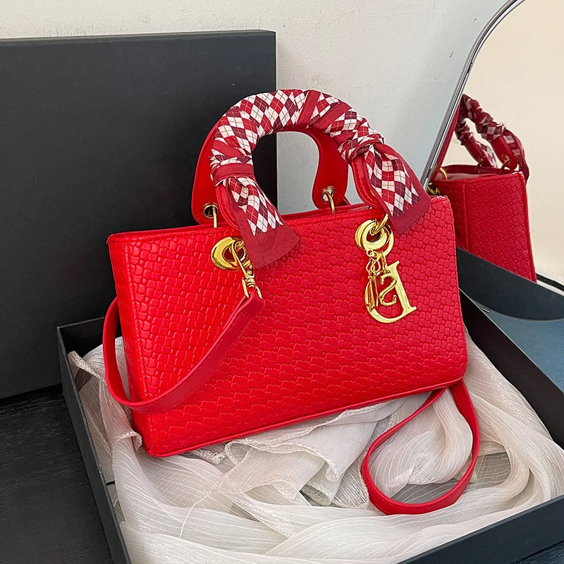 Red handbag with gold clasp and checkered handle in a box