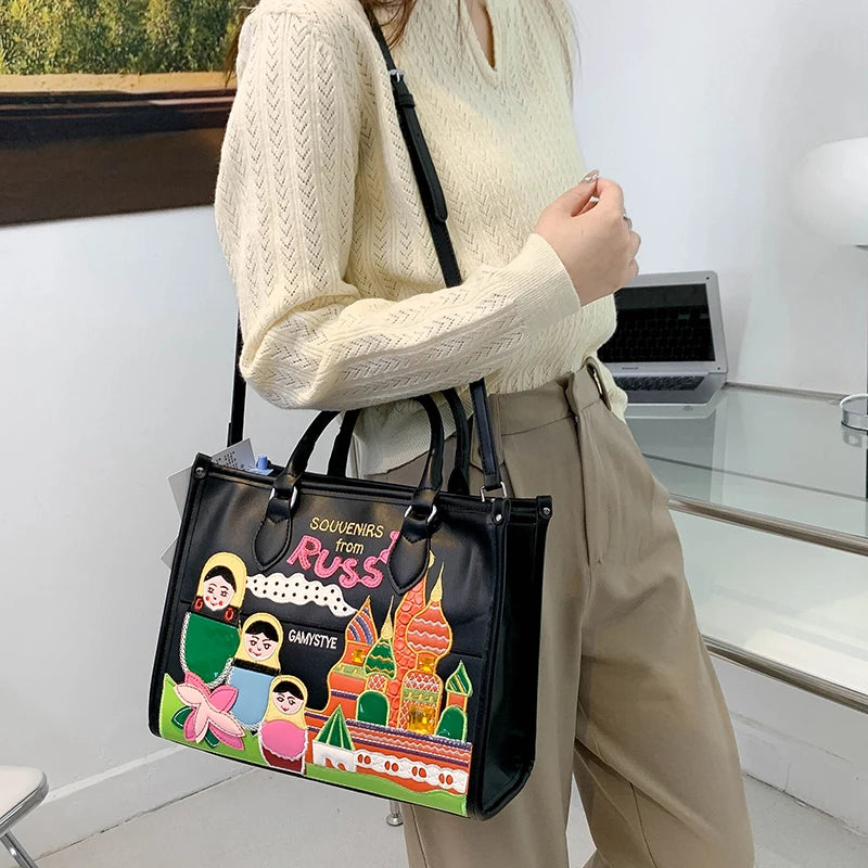 A person wearing a cream cable-knit sweater and beige pants carries a black tote bag with a colorful cartoon illustration and the text 'SOUVENIRS from RUSSIA' and 'SAMSTY'.