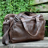 Brown leather duffel bag on a wooden surface with greenery in the background