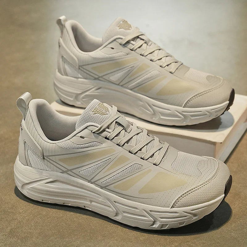 A pair of chunky low-top athletic sneakers in a light beige and off-white colorway, displayed on a neutral textured floor with one shoe resting on a small white box.