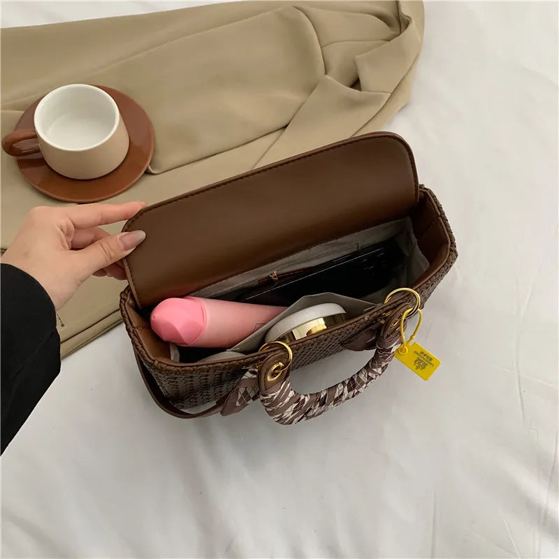 Brown handbag with a visible brand tag, beige coat, and cup in the background
