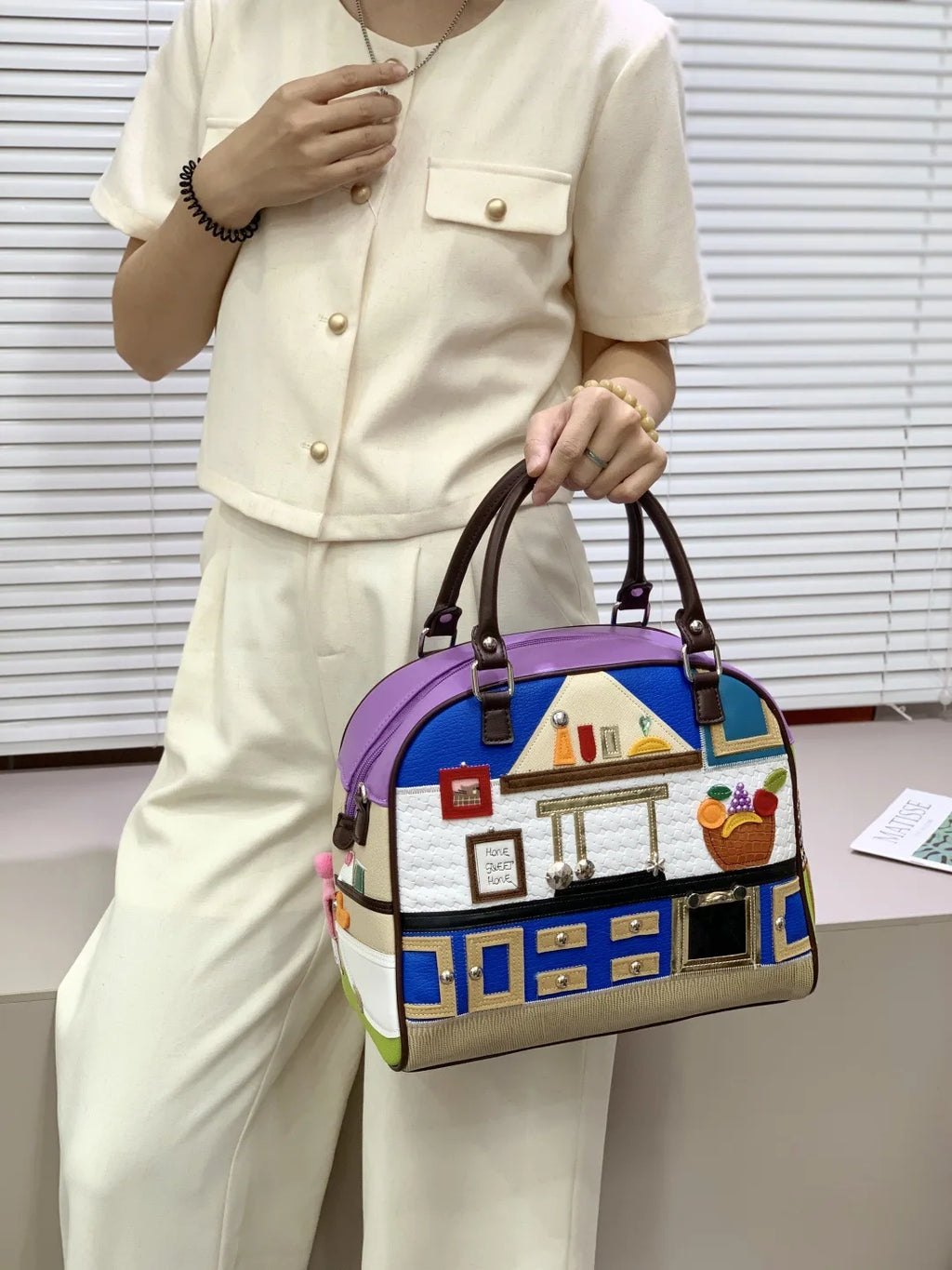 Person holding a colorful handbag with house design against a neutral background