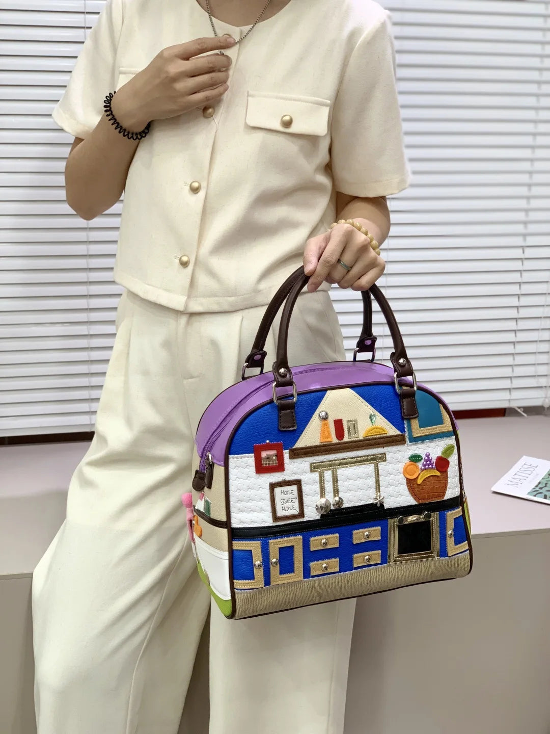 Person holding a colorful handbag with house design against a neutral background