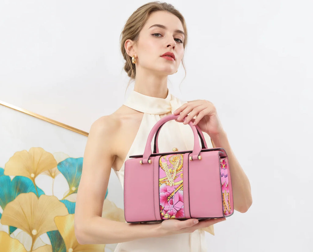 A woman in a cream sleeveless top holds a structured pink handbag with floral and gold patterned panels on the front, set against a clean white background with a decorative gold and blue leaf artwork on the left.