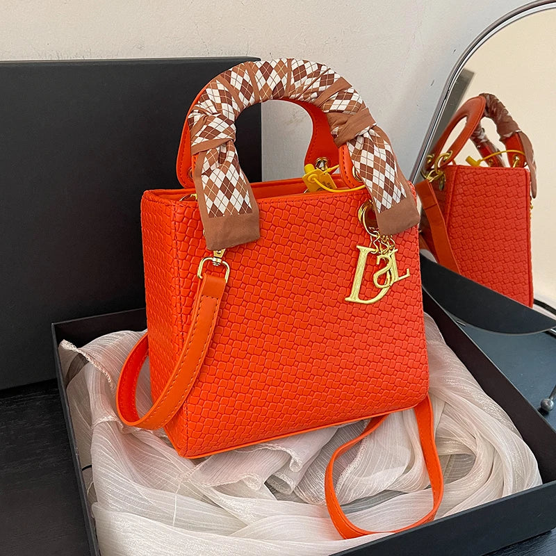 Orange handbag with a checkered handle and gold logo in a box