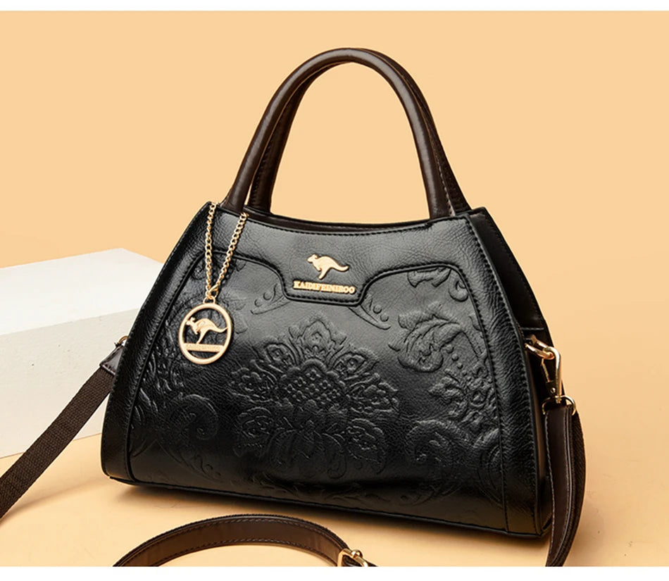 Black handbag with floral embossing and gold accents on a beige background