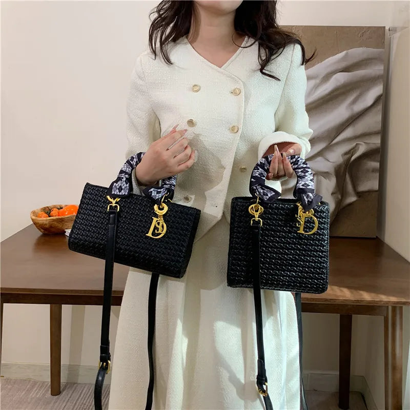 Person holding two black handbags with a gold logo, wearing a white coat.