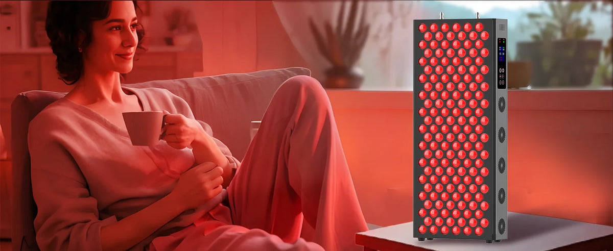 Woman sitting on a couch holding a mug next to a red light therapy device.