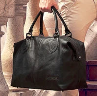 Black handbag held by a person with a blurred background