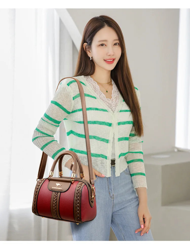 A woman wearing a green and white striped cardigan and light blue jeans carries a burgundy leather handbag with brown straps and gold hardware in a bright indoor setting.