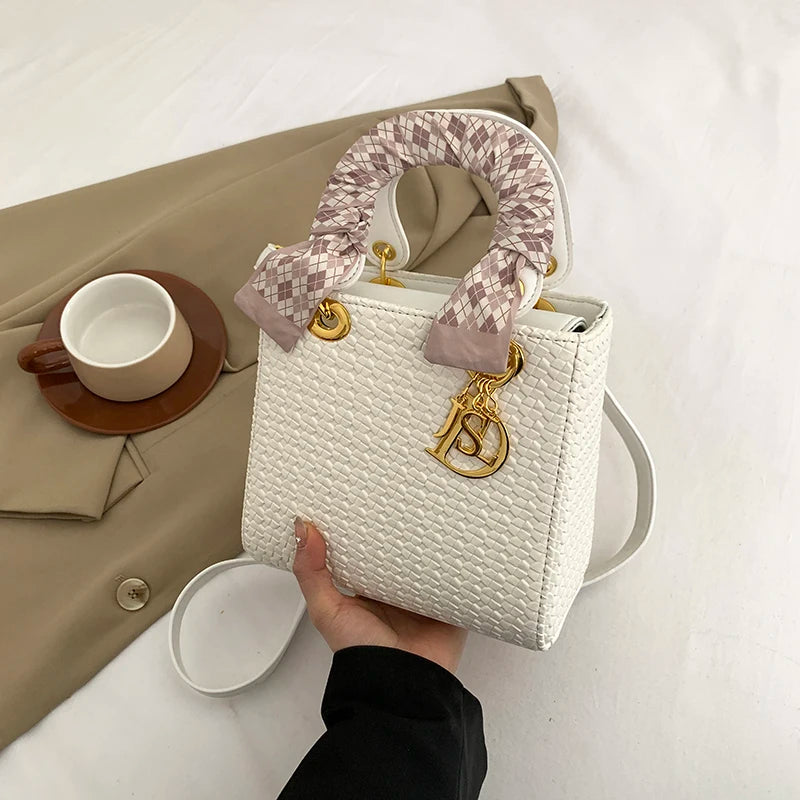 White textured handbag with gold logo charm held by a hand on a neutral background