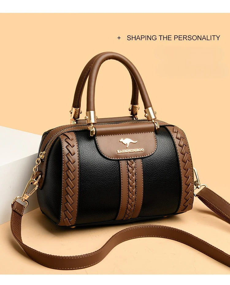 A structured black and brown handbag with gold-tone hardware, featuring a top handle, a detachable shoulder strap, braided side details, and a kangaroo logo patch on the front. The bag is displayed on a warm beige background with a white geometric prop and the text '+ SHAPING THE PERSONALITY' at the top.