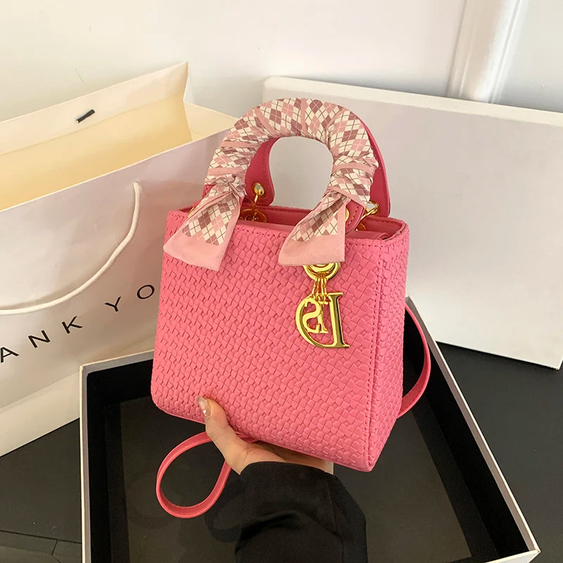 Pink textured handbag with a decorative handle held by a hand, with a brand logo on a white background.