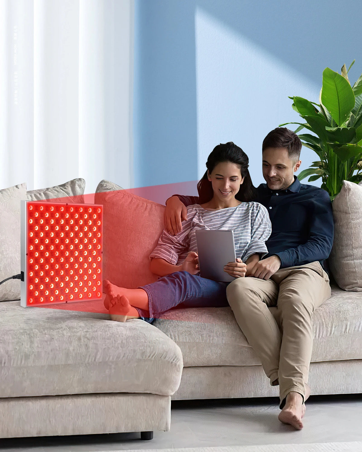Man and woman sitting on a couch with a red light therapy panel in front of them.